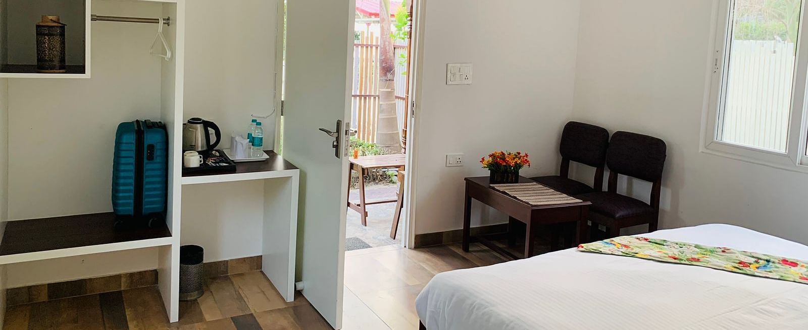 a double bed with pillows and a bed runner on it and chairs opposite it inside one of the rooms - Neer Ganga Resorts