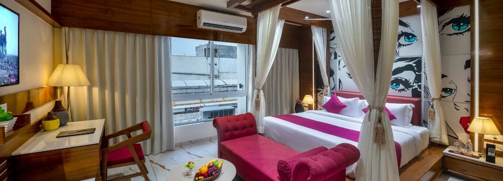 A room with a spacious bed, a small table with chairs, and a window with curtains at Angel Lords Eco Inn Amreli.
