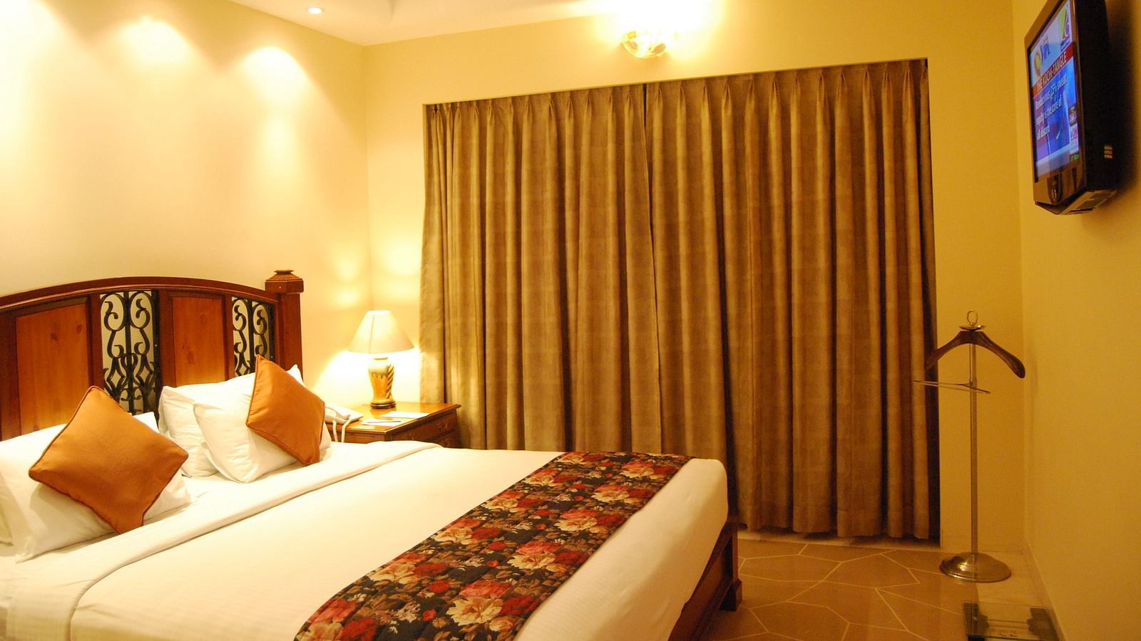 A king bed with a large mattress and cushions, facing a flatscreen TV in a well lit room