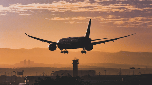 An aeroplane flying in the evening sky with different hues showing in the background.
