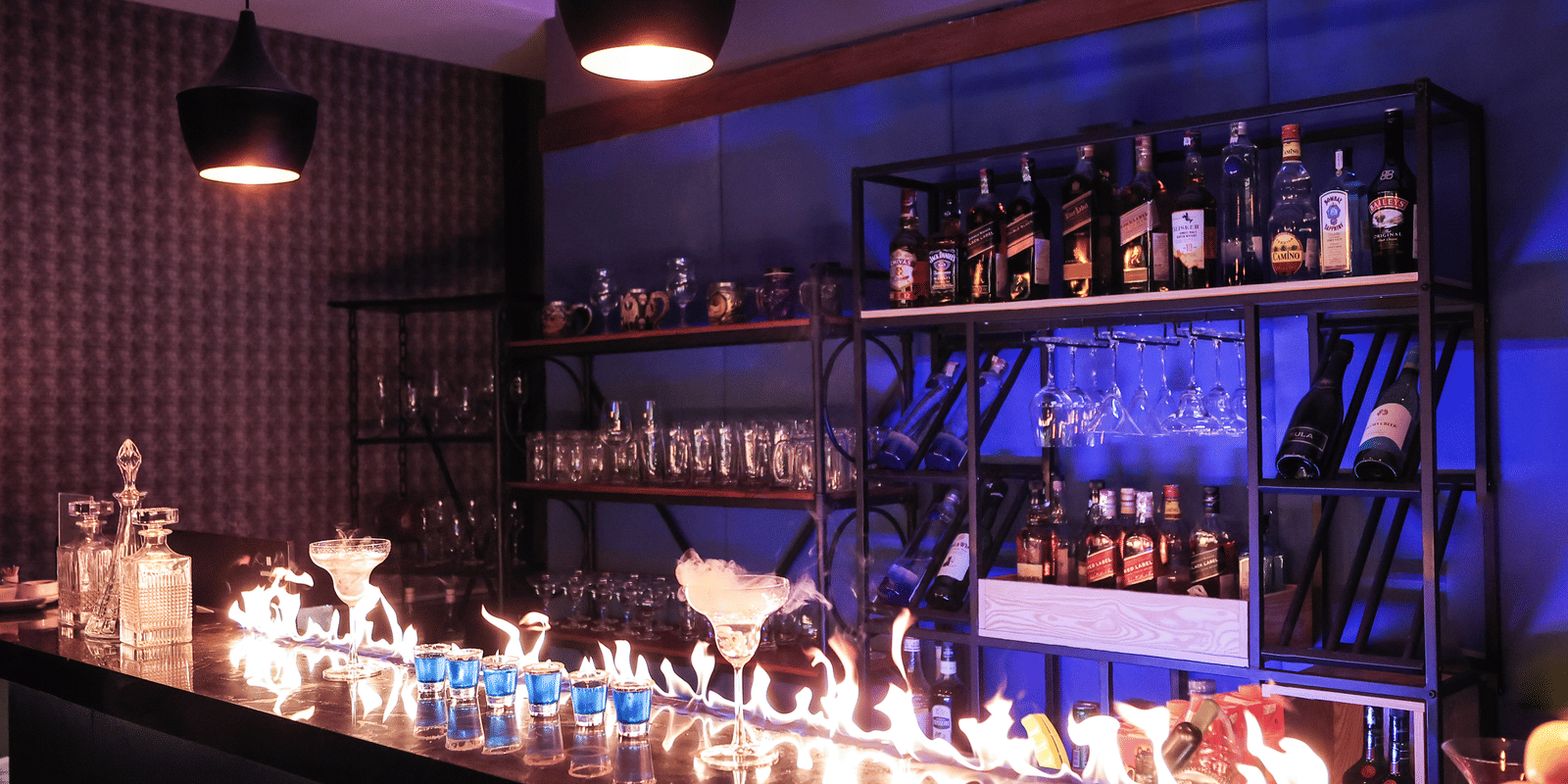 Stylish bar area with bottles on shelving, featuring a long, dramatic flame or dry ice effect across the counter at Hotel Hukam's Lalit Mahal.