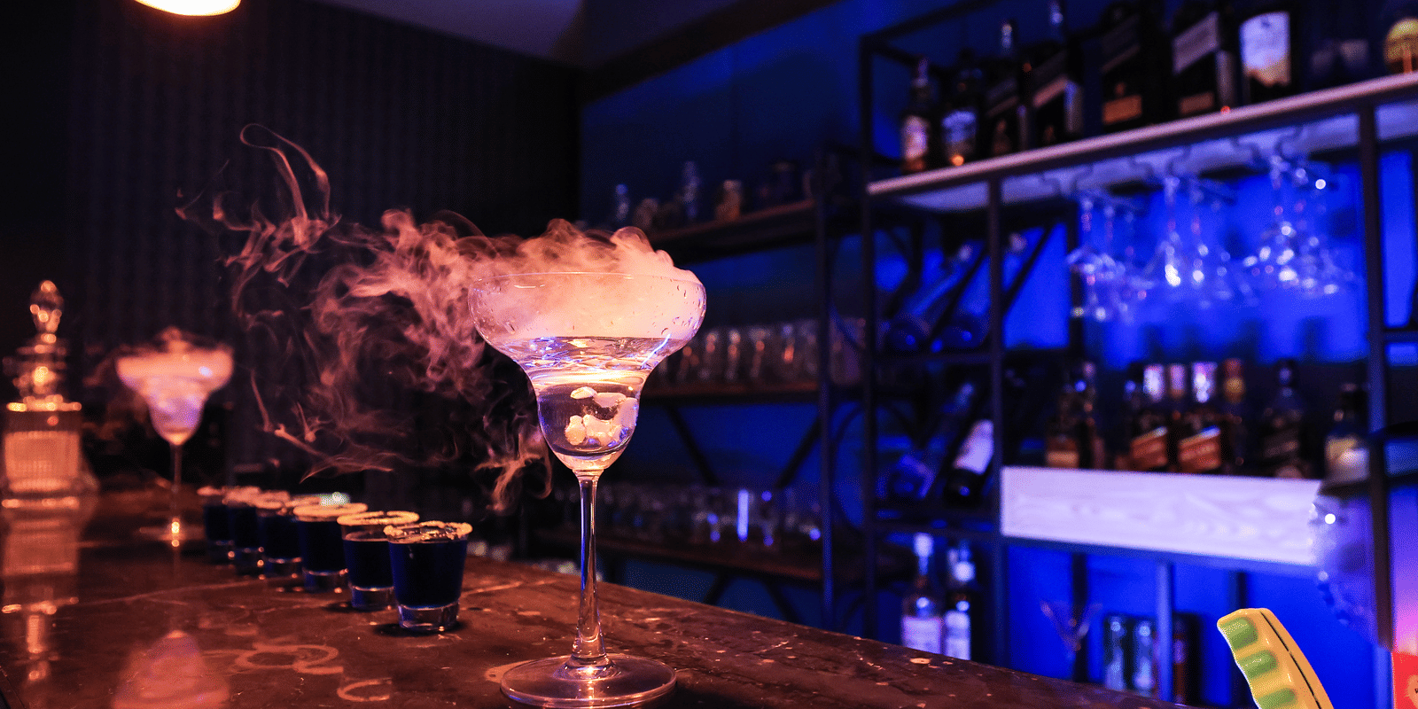 Dramatic bar shot of cocktails lined up with smoky, dry ice effects and strong blue lighting in a dark setting at Hotel Hukam's Lalit Mahal.