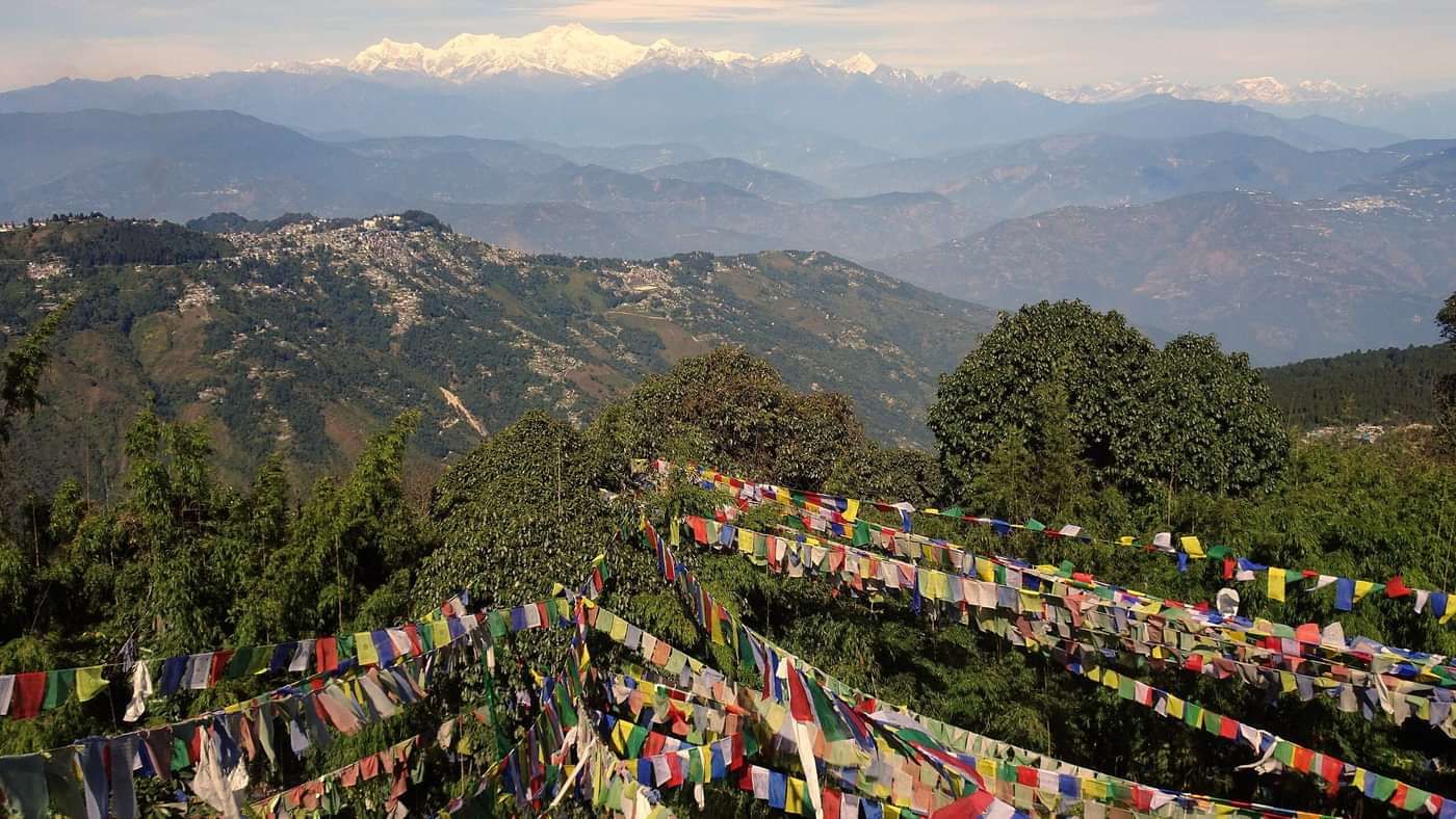 Colourful prayer flags fluttering in the wind, overlooking a panoramic view of valleys and distant mountains.