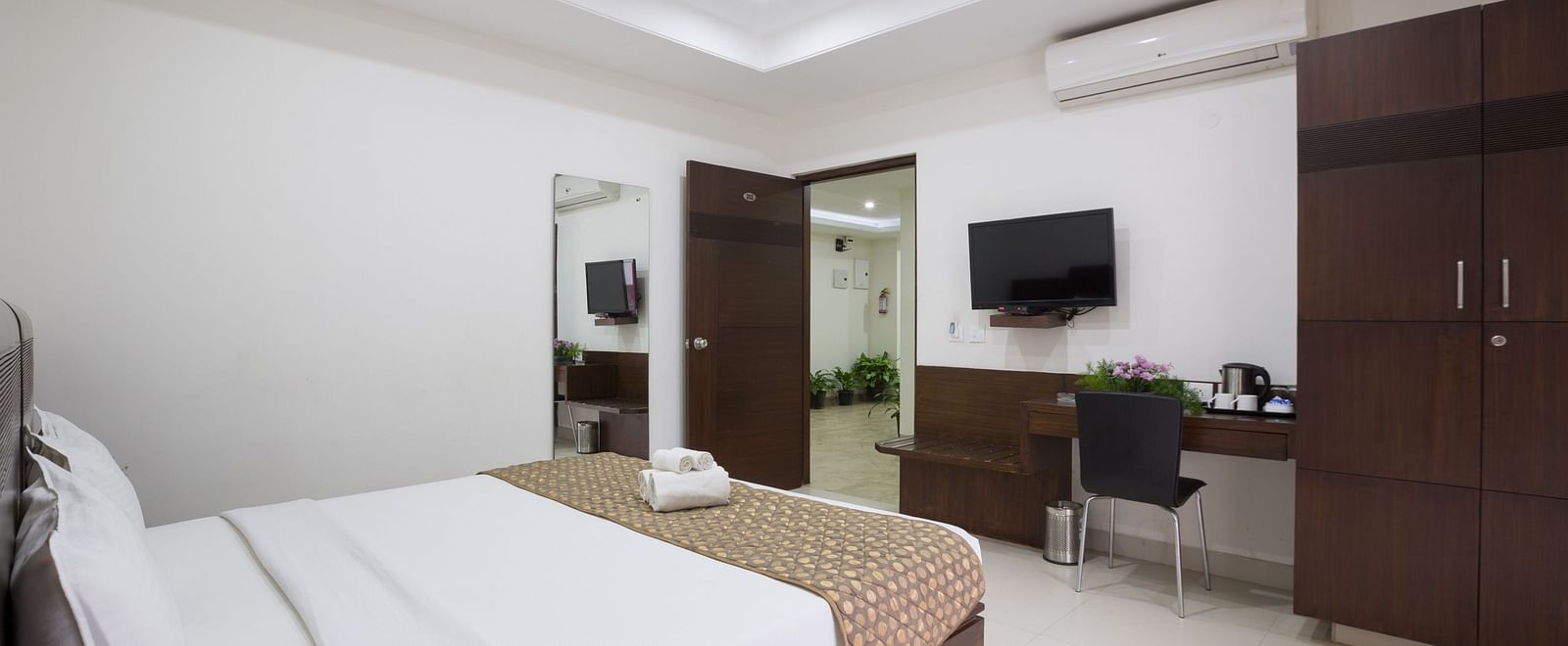A room with a bed, a desk area, wardrobe, and a television mounted on the wall - Sanctum Suites BEL Road, Bangalore