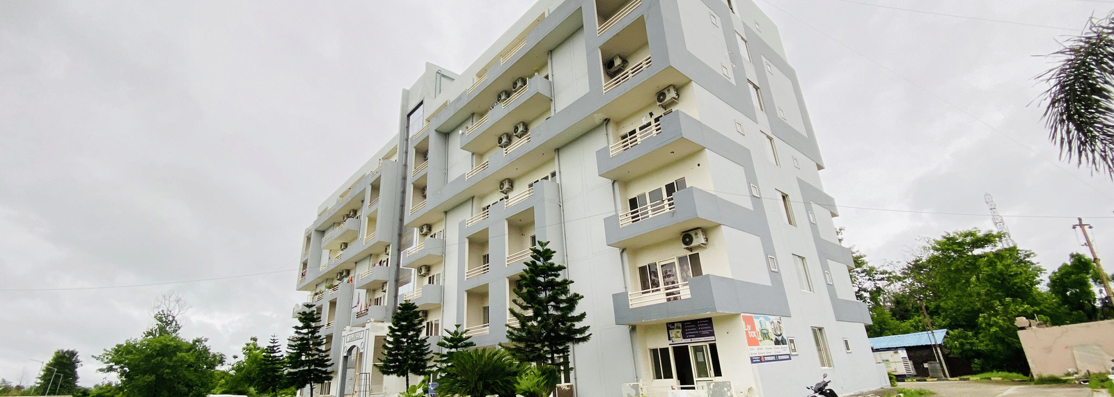 The facade of multi-storey Livbox, Rudrapur featuring the balconies, greenery, and a curved driveway in the foreground.