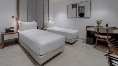 A well-lit Standard Room featuring two twin beds, a desk, and a chair. - The Pelican Hotel, Accra