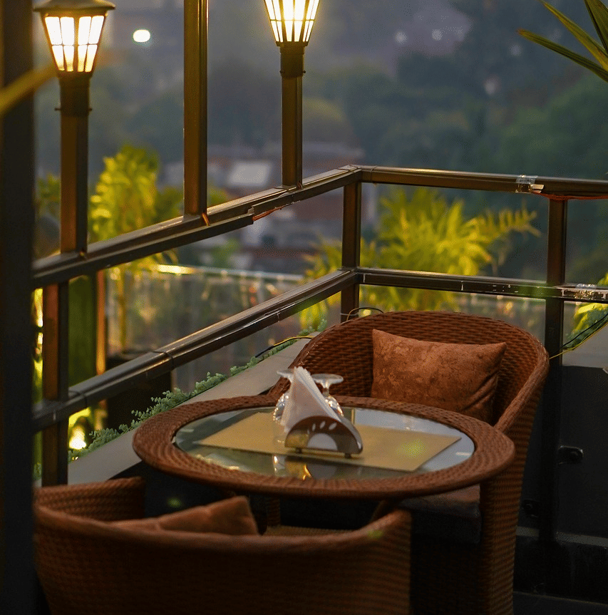 Two chairs facing each other on a terrace with warm lights besides it on a late evening.