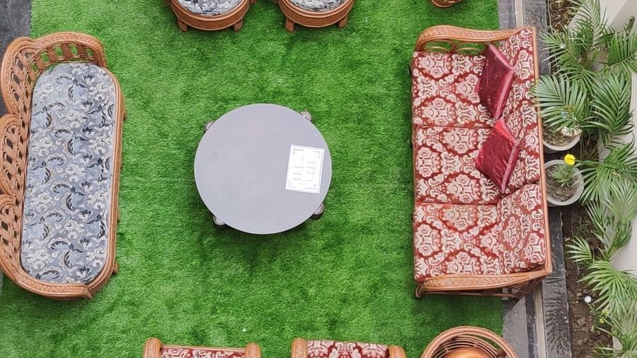 An aerial view of an outdoor seating area at Hotel Exotic Amritsar, showing several wicker chairs and a table arranged on a green rug.