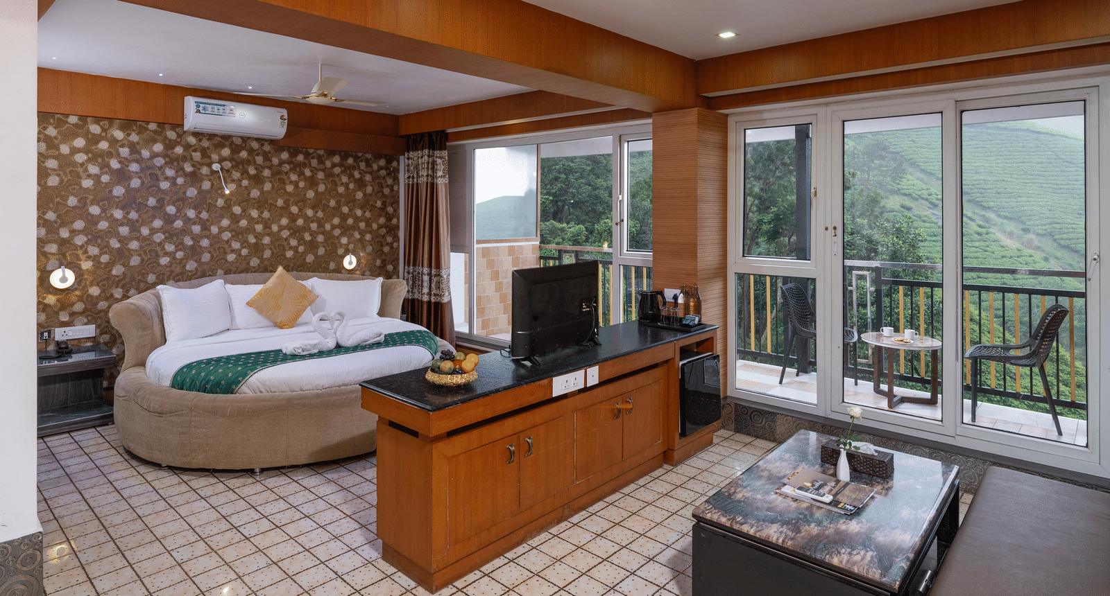 The interior of the Honey Moon Suite at Parakkat Nature Hotel and Resorts, Munnar, featuring a large round bed, seating area, ceiling fan, and sliding doors leading to a private balcony with landscape views.