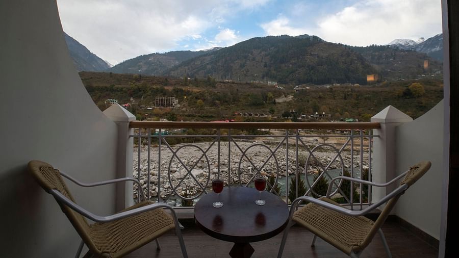 A balcony with two chairs and a table facing a river view - Mastiff Grand, Manali
