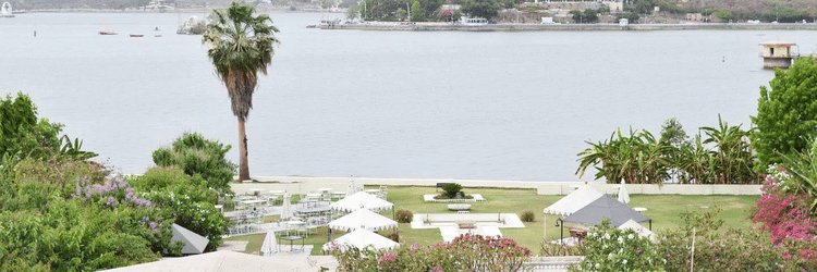 A panoramic view of a lake from Ram Pratap Palace, showing the garden event space with dining tables and tents, with hills in the background.