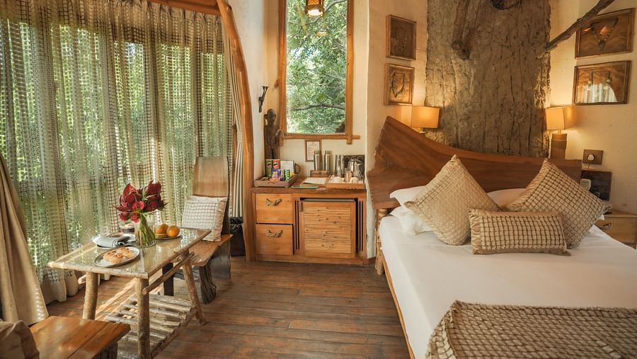 A bedroom with a bed, a lamp, and warm lighting, large windows - The Den Corbett Resort & Spa, Kumeria.
