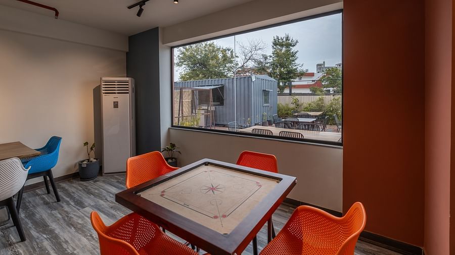 Game room at Clarks Inn Suites Jaipur, Ajmer Road features a carrom board surrounded by 4 chairs placed by the window and a cooler placed in the corner.