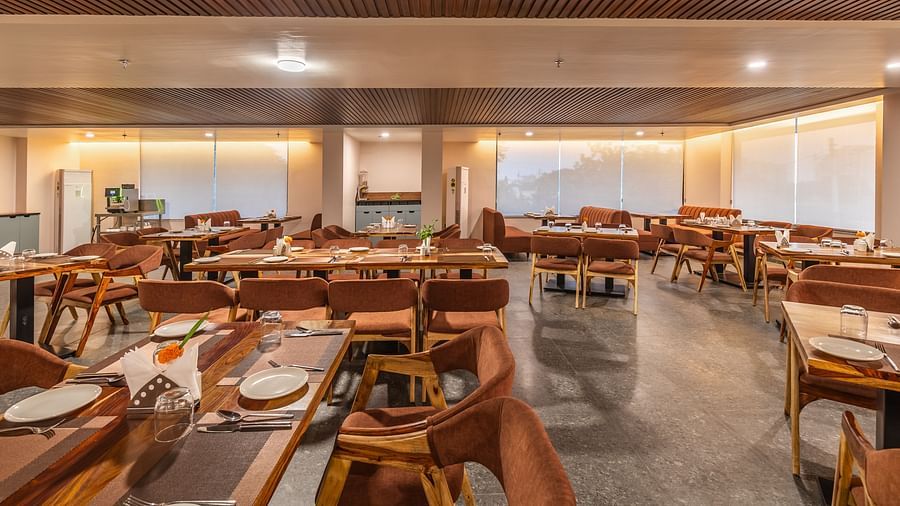 Well-lit restaurant with neatly arranged tables, wooden chairs, and large windows at Clarks Inn Suites Jaipur, Ajmer Road