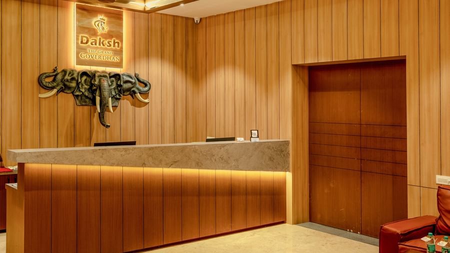 The front desk at the lobby of Daksh The Grand Goverdhan, Dwarka, with a huge wooden door beside it.