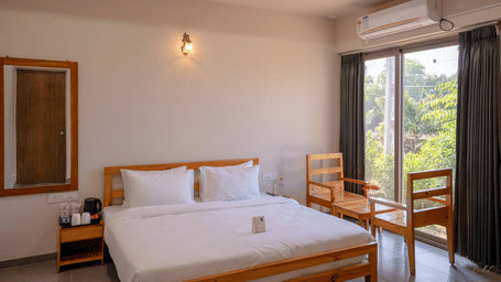 A cosy bedroom view highlighting the wooden bed frame, bedside table, and air conditioning unit under warm wall lighting - Daksh The Nirvana Retreat, Pavagadh