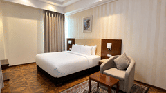 Suite bedroom with king bed, white linens, parquet floor, Persian rug, armchair and decorative ceiling light at Golden Tulip Kukas