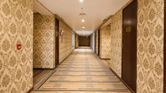 Long hotel corridor at Golden Tulip Kukas Jaipur with patterned carpet flooring, recessed ceiling lights, and decorative wallpaper lining both sides.