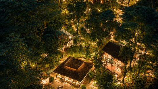 Aerial twilight view of the warmly-lit resort structures nestled within a dense forest at Neemrana's Glasshouse on The Ganges - 21st Century, Rishikesh.