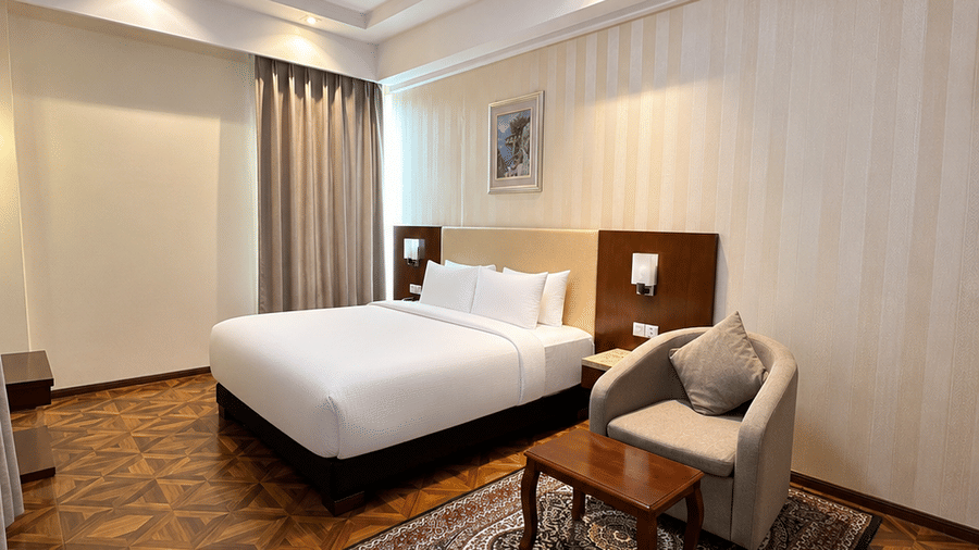 Suite bedroom with king bed, white linens, parquet floor, Persian rug, armchair and decorative ceiling light at Golden Tulip Kukas