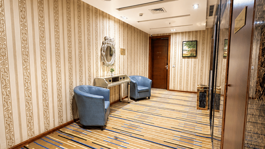 Hotel corridor at Golden Tulip Kukas Jaipur featuring striped patterned carpet, beige curtained walls, and recessed ceiling lights.