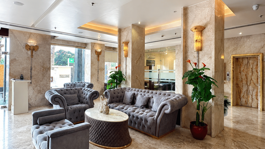 Bright hotel lobby lounge at Golden Tulip Kukas Jaipur with cushioned seating, indoor plants, marble flooring, and natural light from large windows.