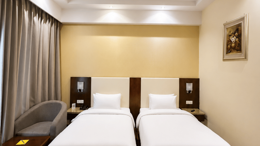 Superior Twin room at Golden Tulip Kukas Jaipur showing two neatly made single beds, framed wall art, striped carpet flooring, and soft ambient ceiling lighting