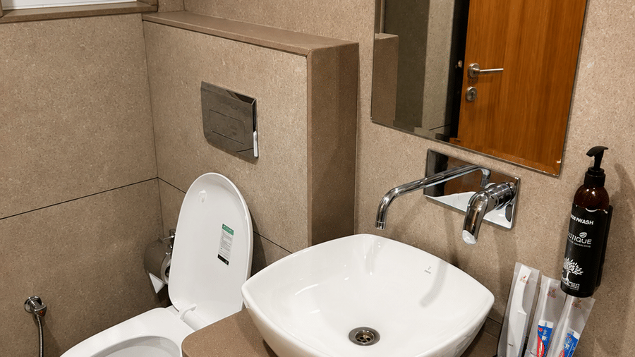 TGI Apple Inn, Ajmer Road, Jaipur | A bathroom with a sink, a toilet seat, a door, and a  towel.