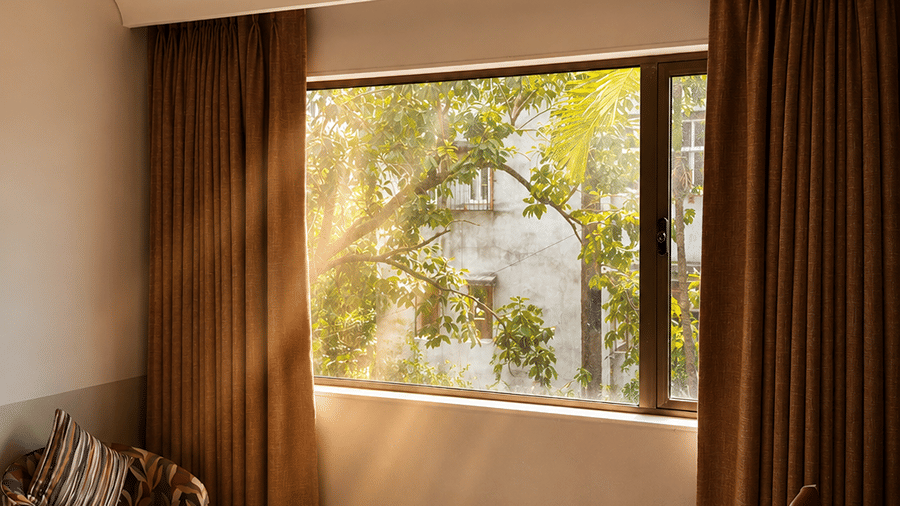 A seating space with a cushion, a table, and a window partially covered with curtains. | The Oriental Residency