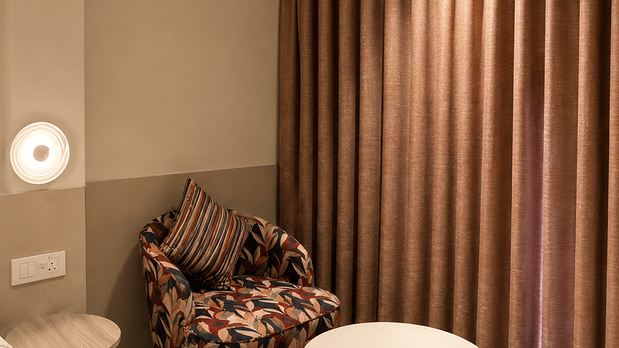 A seating space with a cushion, a table, and a window covered with curtains. | The Oriental Residency