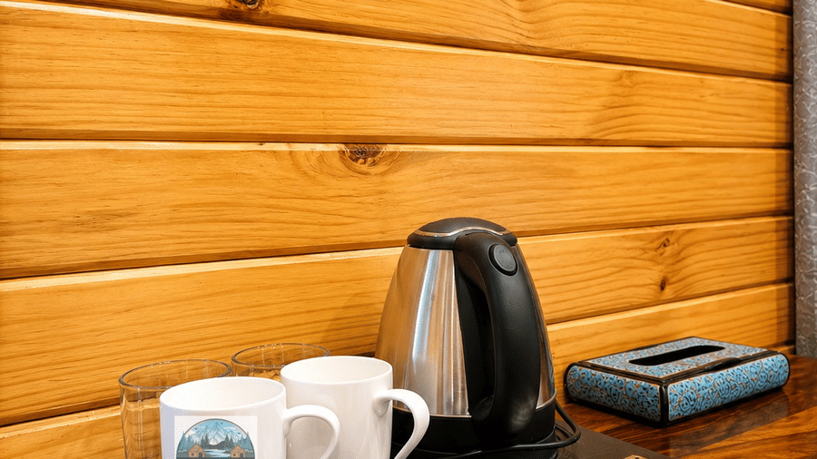 A tea & coffee maker tray at Dawat e Drung by FrozenFall Resort, Drung, Tangmarg, featuring a kettle, 2 mugs, and packets of condiments.