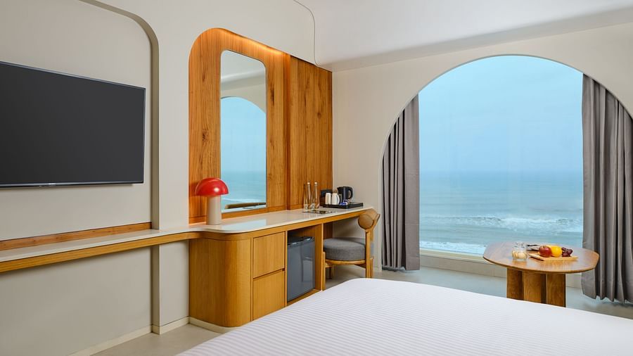 Image featuring a huge TV mounted on the wall next to which a dressing table cum work desk is placed and a huge window with a breathtaking view of the sea