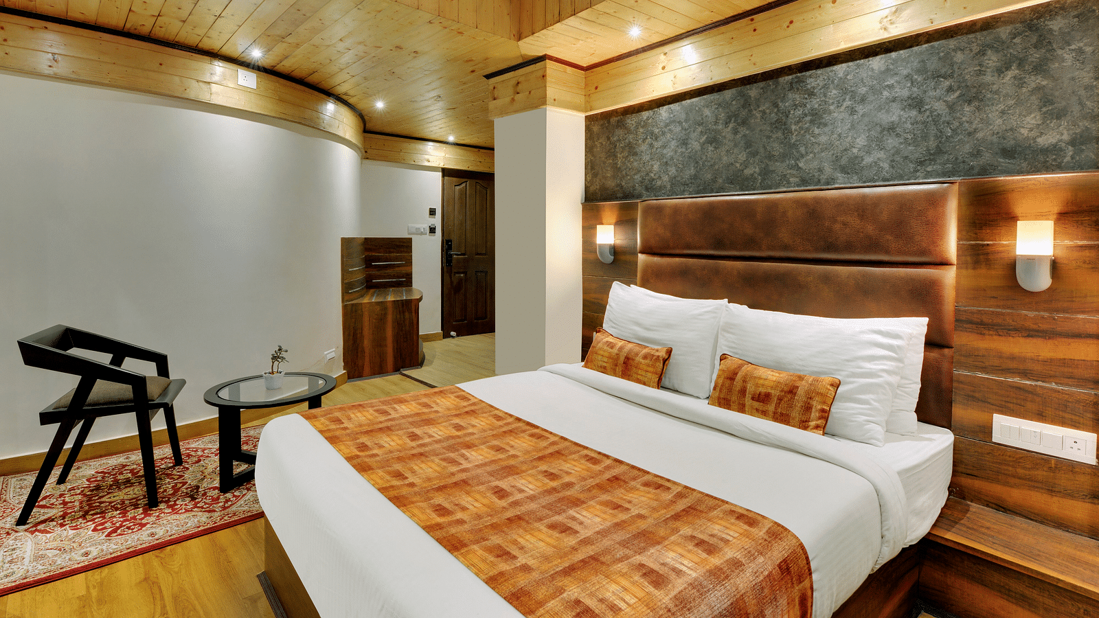 An image of Sumitel Queensyard deluxe room with king size bed, a chair and a table and minimal decoration