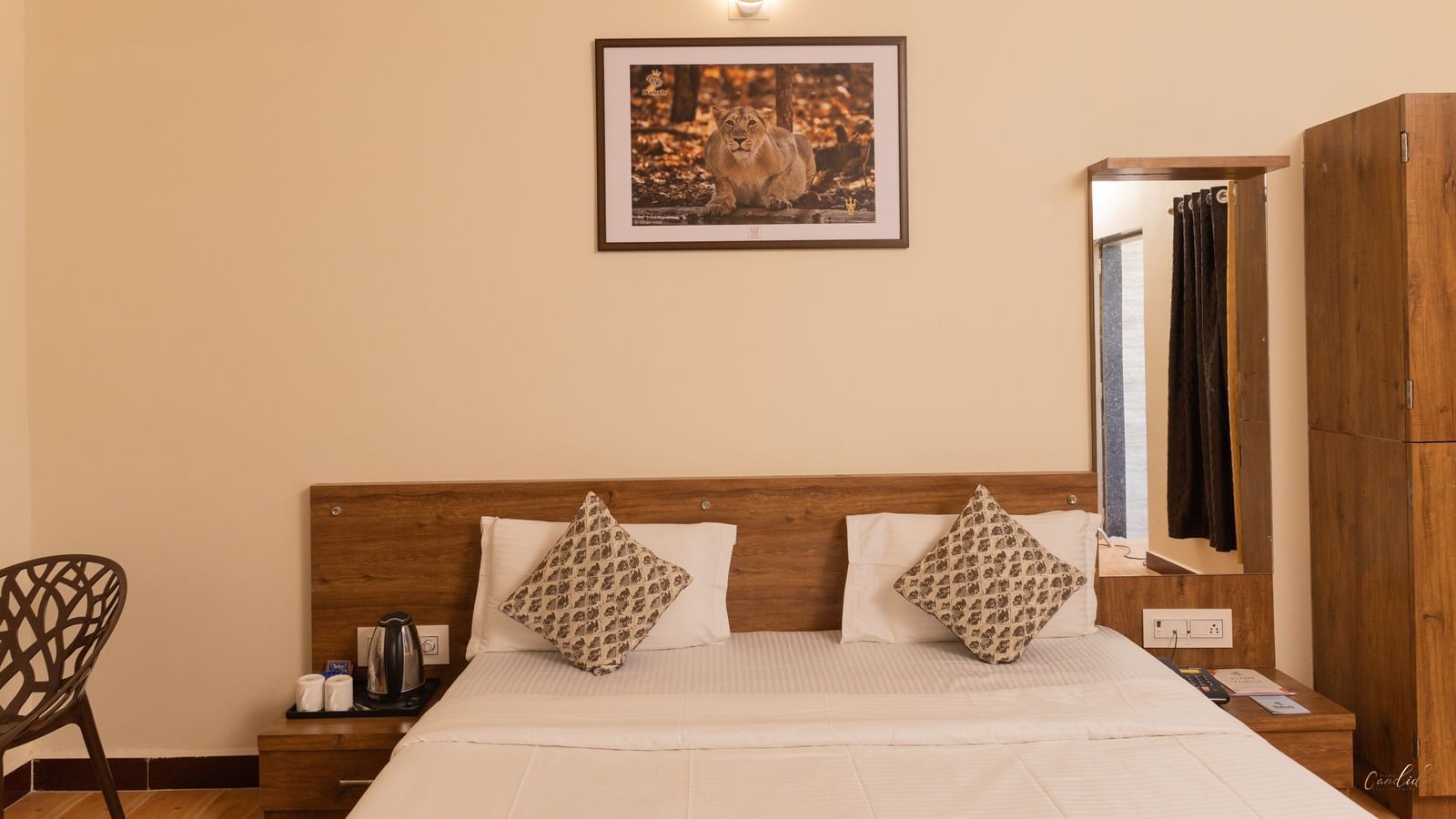 A close-up of a bed with brown accents, a wall art, a wall mirror, and a wooden wardrobe at Daksh Resort & Amusement Park, Sasan Gir.