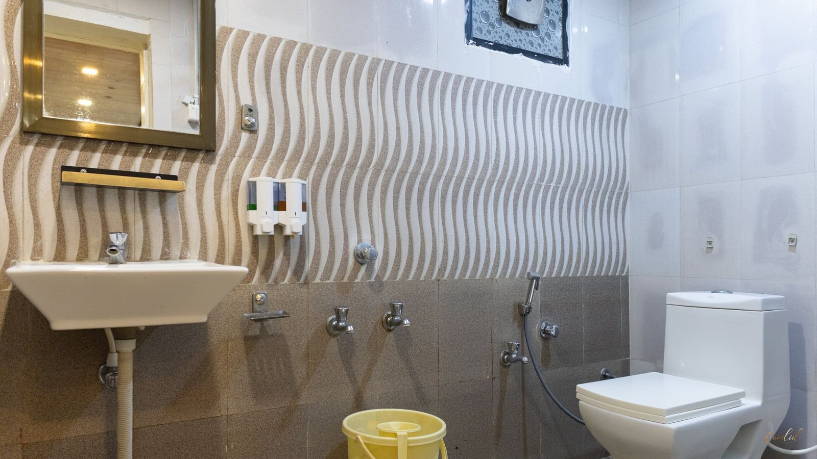 A modern bathroom with brown wave-textured tiles, a square mirror, a sink, and a toilet, at Daksh Resort & Amusement Park, Sasan Gir.