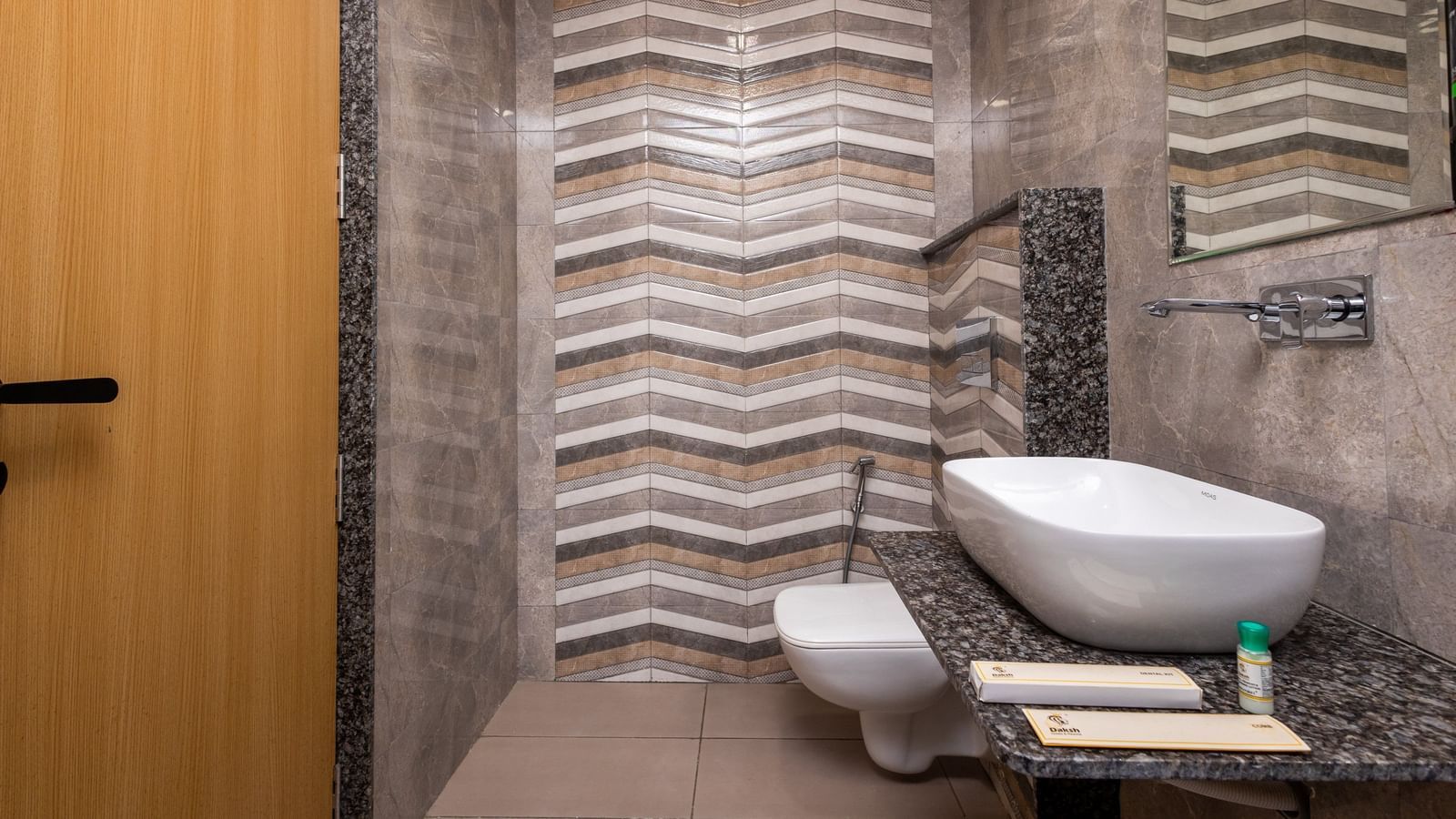  A bathroom at Daksh The Grand Gowardhan, Dwarka, showcasing chevron tiles, a toilet, and a sleek wash basin with new utilities.