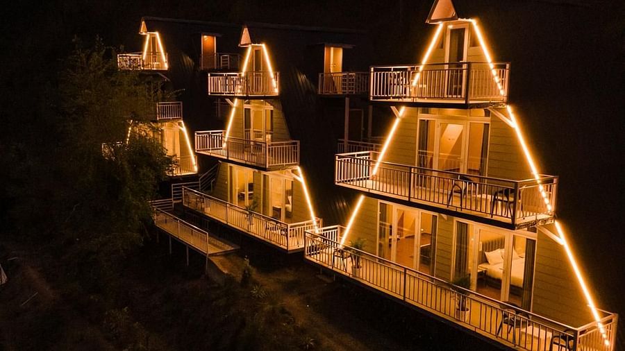 An aerial night view of a resort with several A-frame or pyramid-shaped cottages illuminated with warm lights.