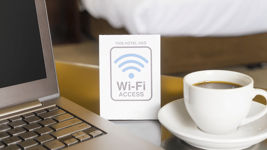 Close-up of a laptop next to a cup of hot coffee and a complimentary Wi-Fi access sign.