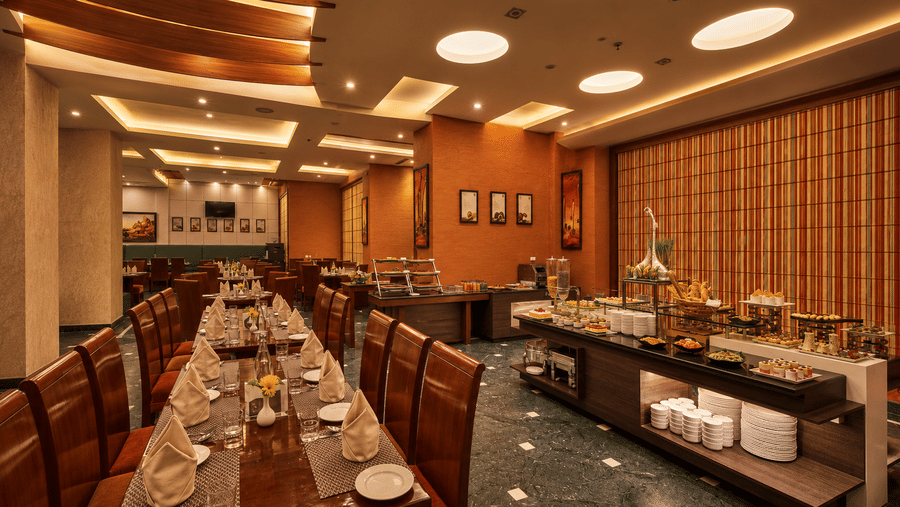 Elegant hotel restaurant with buffet spread, leather chairs, striped walls, and warm ceiling lights.