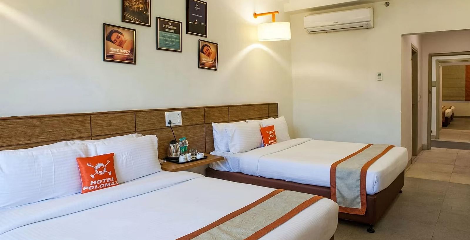full view image of the max family room featuring two plush double beds along with a split air-conditioner and a bedside table between the two beds - Max Hotel Jabalpur