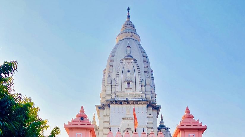 a white and pink temple in the distance with the pathway next to trees and blue sky in the background.