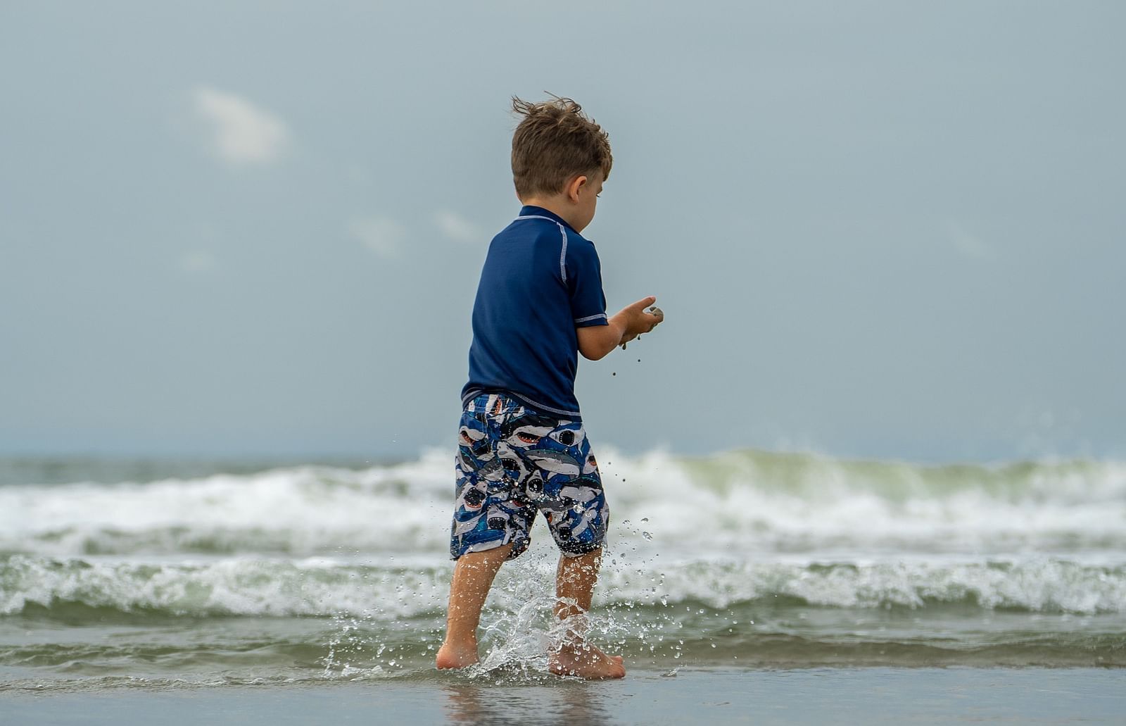 An overview of a child playing in the beach with the waves overlapping.