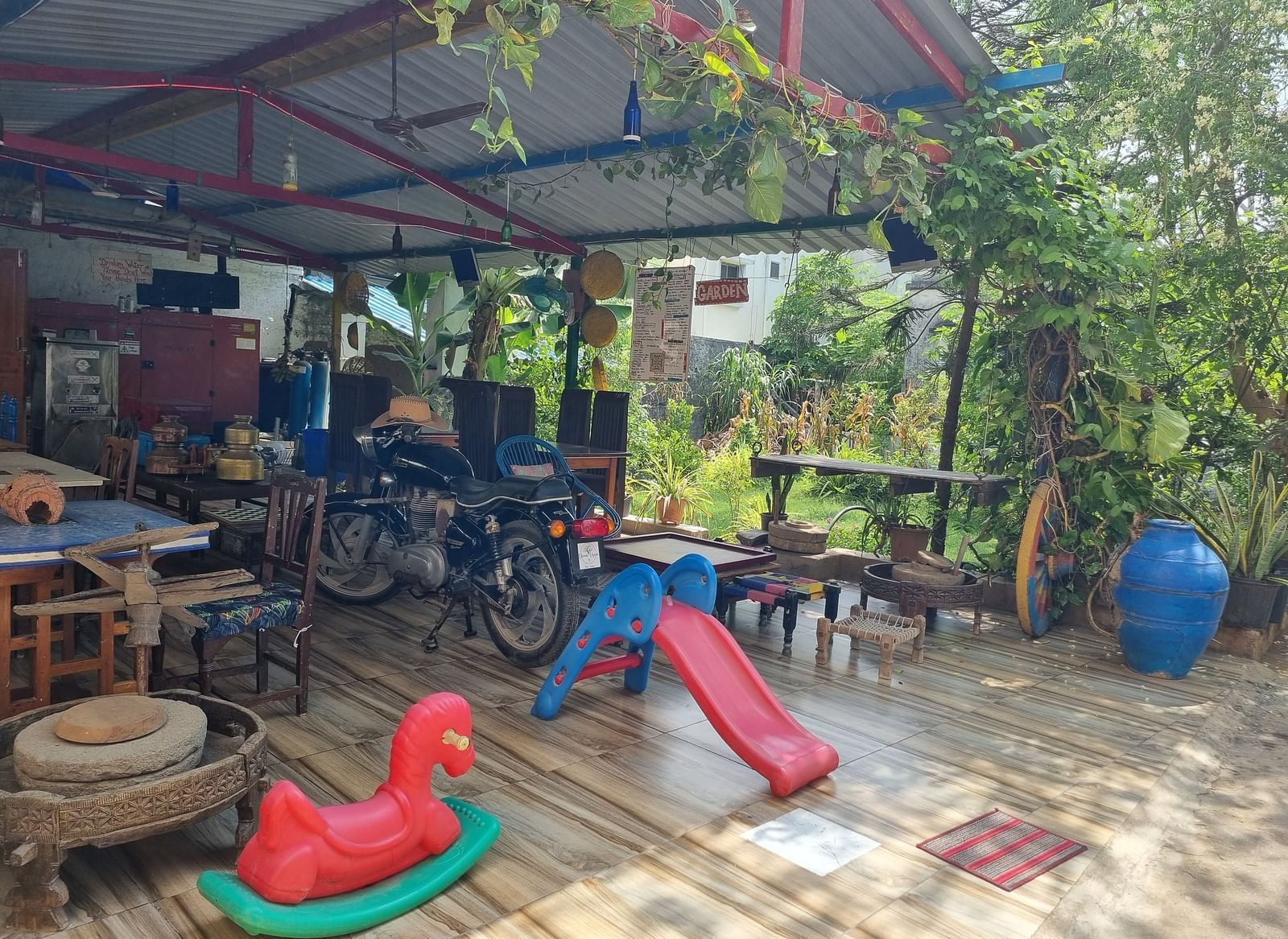 The kids' play area with surrounded by lush greenery along with a motor cycle kept under the shed at Dream Vision Guest House.