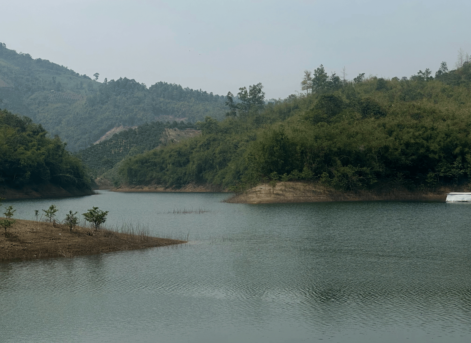 Scenic lake surrounded by hills and greenery with calm water and natural landscape in view.