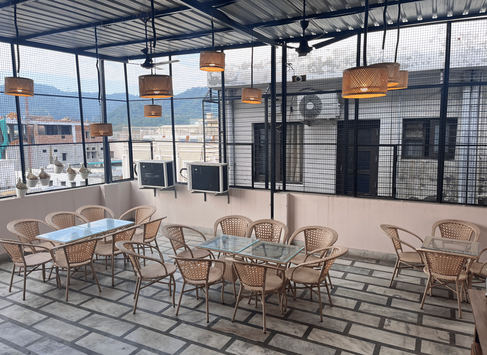 Full view of the rooftop restaurant at Perfectstayz Value Dhruv Nanda, Haridwar, with warm lights hanging from the tin ceiling along with a beautiful mountains in the background.