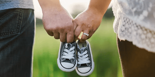 Couple holding baby shoes, symbolising pregnancy announcement or baby shower celebration in a scenic outdoor setting.