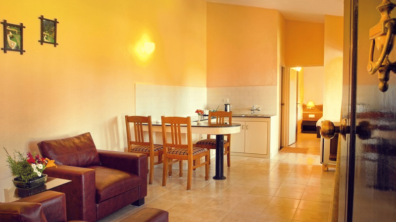 Living and dining area featuring a sofa, wooden dining table and chairs, beige tile flooring, and light yellow painted walls at Green Pastures, kodaikanal.