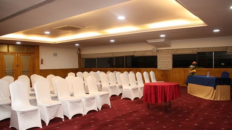 An image showing the chairs facing the dais, with a small round table with red table cloth, beside a small desk and chair - Monarch Hotels