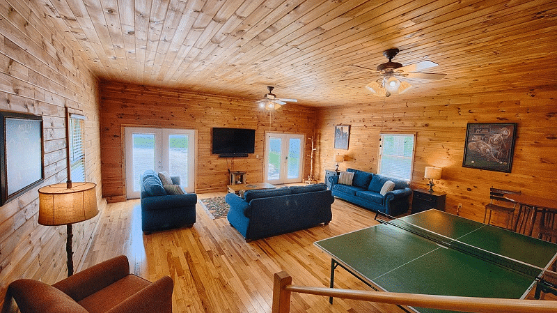 the living area of the river house with wooden interiors featuring a ping pong table and a seating area with blue couch set - Historic Tapoco Lodge
