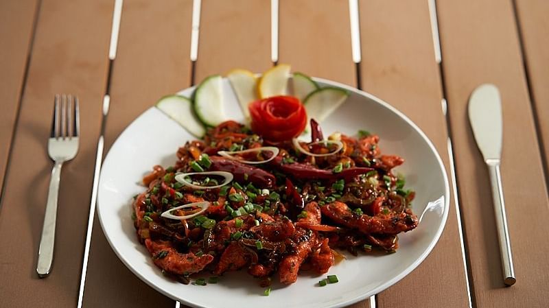 A white plate of  vegetables garnished with fresh herbs and a carved tomato rose, served with sliced cucumber and lime, placed on a wooden table with a fork and knife at The Hamuse Hotel, Kodaikanal.